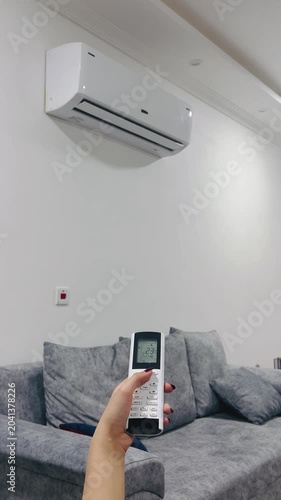 Turning on the air conditioner with a remote control, 9:16 vertical video, adjusting climate control, home comfort, cooling the room, modern HVAC system, lifestyle.