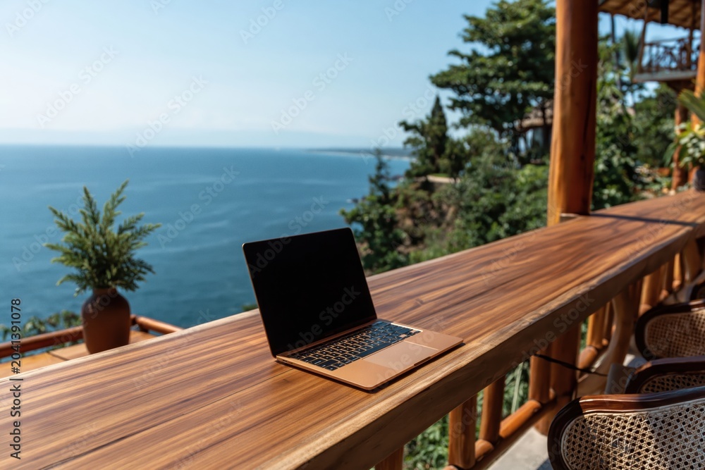 Fototapeta premium Laptop computer on wooden deck terrace with tropical ocean view technology