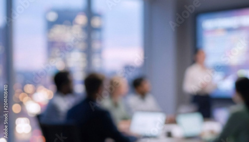 A blurred image of a corporate meeting in a modern office setting. Participants are engaged in a presentation with a city skyline in the background.
