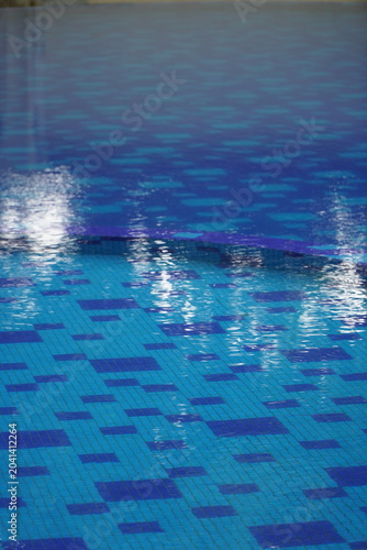 A vertical shot of the same swimming pool, capturing the same mosaic-tiled floor and shimmering water surface