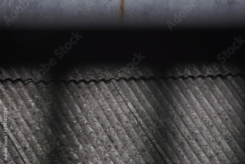 A close-up horizontal shot of an old corrugated asbestos/cement roof, captured from a low angle showing the wavy, ridged surface texture in detail