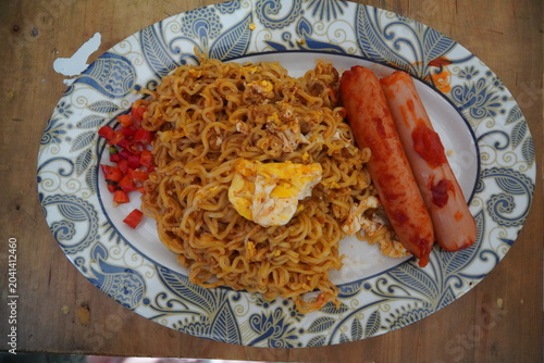 A plate of Indonesian stir-fried instant noodles (Mie Goreng) served on a decorative blue and white oval plate with batik/paisley pattern