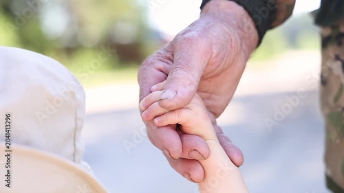 A toddler walks hand in hand with his grandfather. Close-up of his hands.