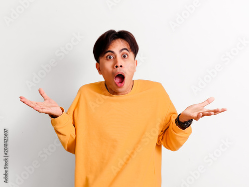 Konstfotografi A surprised young Asian man in a yellow sweatshirt reacts with a wide-eyed jaw-dropping shocked expression while gesturing with open palms