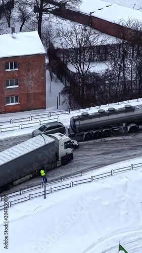 Aerial vertical parallax shot of winter truck accident with jackknifed trailer on slippery icy road and yellow rescue tractor arriving in Latvia