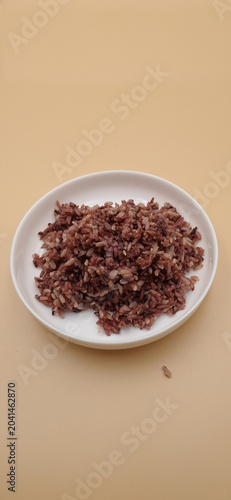 Steamed organic black riceberry in a white ceramic plate on a beige background.