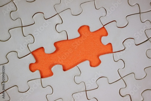 Close-up of white puzzle pieces with one missing section revealing orange background, symbolizing problem solving, connection, teamwork, and copy space for text.