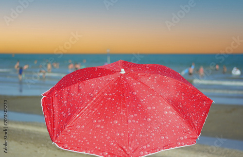 Open umbrellas on a deserted beach as the sun sets on the horizon
