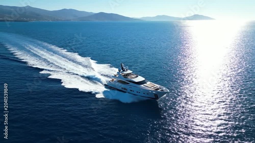 Luxury motor yacht cruising at high speed across blue ocean water under bright midday sun with mountain coast