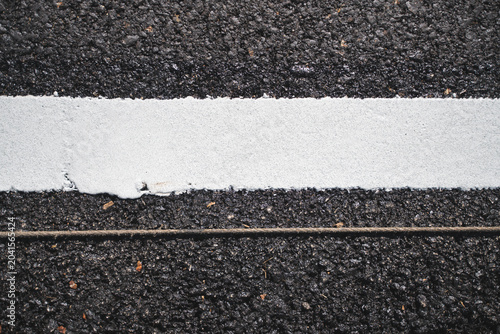 Close-up of a freshly painted white line on a black asphalt road, highlighting the texture and contrast between the two surfaces.