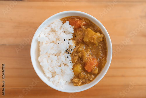 White rice with black sesame seeds and vegetable curry in a bowl on a wooden surface.