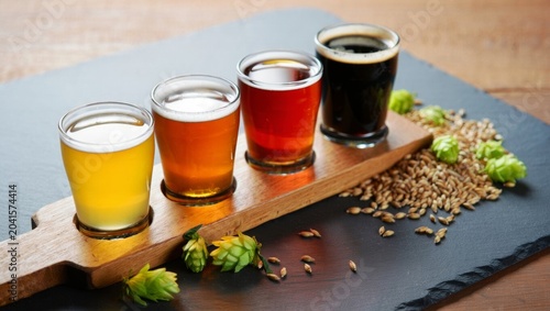 Beer Tasting Flight with Four Different Beers on Wooden Paddle with Hops and Barley