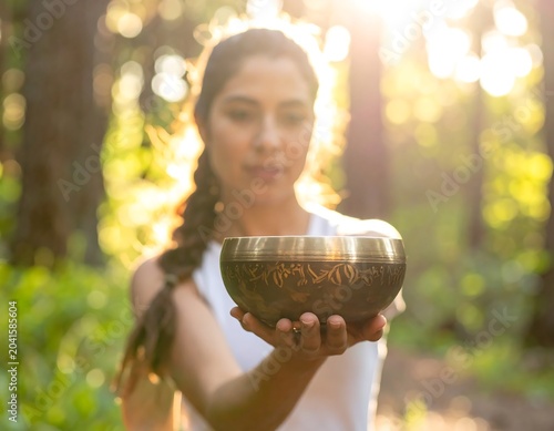 Young Woman Holding Brass Singing Bowl in Sunlit Forest Clearing