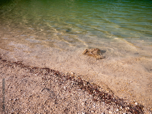 Clear water on a gravel shoreline at a flooded quarry lake in Kralovany, Slovakia. Shallow freshwater with visible bottom, small stones and natural lakeside texture.