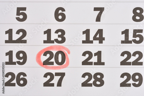 Close up of a white calendar sheet with black date numbers and a hand drawn red circle around twentieth day