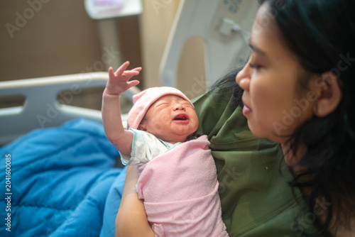 Mother holding crying newborn baby in hospital bed after childbirth