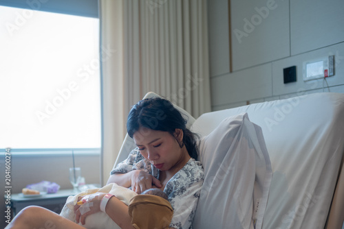 Asian mother breastfeeding her newborn baby girl in hospital bed after delivery