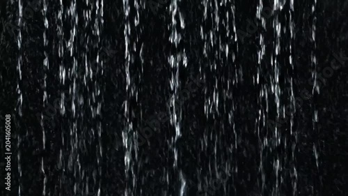 Water droplets fall rapidly down a dark surface creating a mesmerizing display