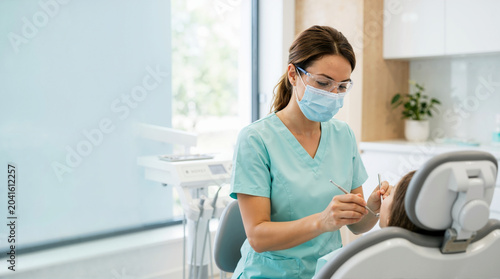 Female dental hygienist in mask and safety glasses treating a patient. Professional dentist working in a modern dental clinic. Oral healthcare concept