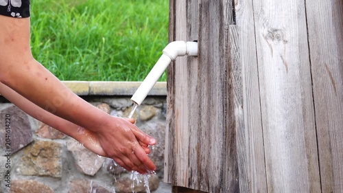 The girl washes his hands at the well. White plastic crane. Wooden well with automatic water flow.