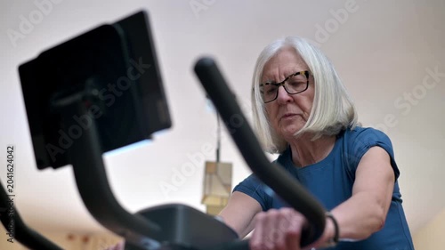 Senior Woman Exercising On Stationary Bike At Home Focused On Fitness 