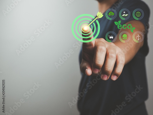 Eco target concept with finger pressing green bullseye and sustainability icons showing renewable energy, recycling, tree planting and low emission transport renewable energy
