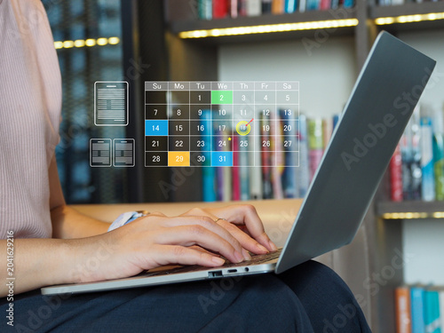 Woman typing on laptop with transparent digital calendar overlay showing scheduled dates and icons, focused on planning and productivity in cozy library workspace