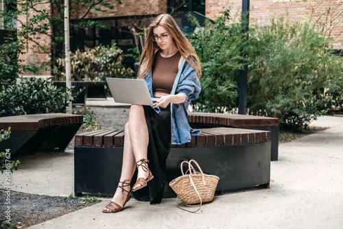 Fotografie Woman uses laptop while sitting on wooden bench outdoors