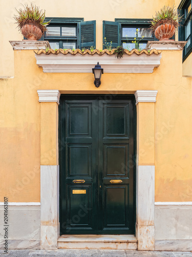 Historic yellow facade with a dark green entrance door and potted plants in the charming Plaka district, Athens.