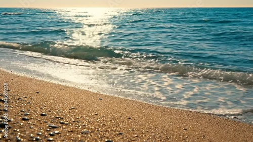 Waves gently lapping the golden sandy shore on a bright sunny day creating a peaceful beach scene.