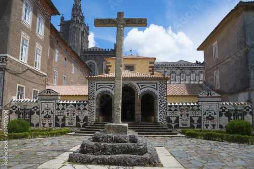 Ein altes Steinkreuz steht im Hof vor einem Mosaikdekorierten Gebäude unter blauem Himmel, ehemaliges Klosters, Convento de Santa Cruz, Mata Nacional do Buçaco, National-Wald von Bussaco, Bucaco, Mealhada, Beira Litoral, Portugal