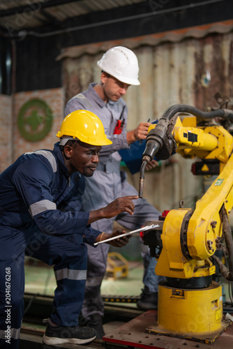Workers examine a yellow robotic arm