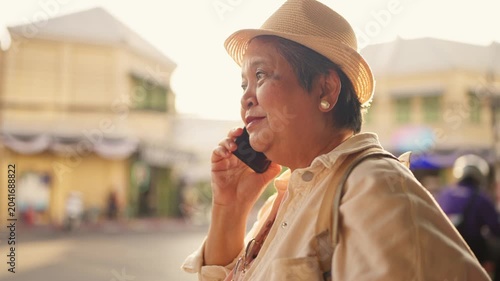 Asian senior woman talking on phone call while exploring city outdoors. 