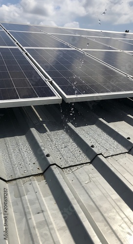 Wet Solar Panels Mounted on Gray Metal Roof Under Cloudy Sky