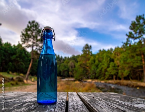 Blue Glass Bottle Standing on Weathered Wooden Table Beside Forest River