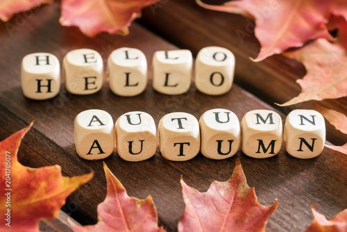 Hello autumn inscription and red maple leafs on wooden background, selective focus