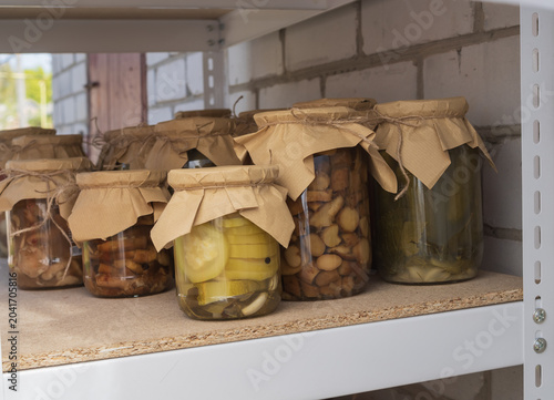 Canvas Print Collection of preserved vegetables, mushrooms, cucumbers, peppers, and tomato products in glass jars stored on shelves