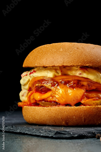 Gourmet vegetarian burger with melted cheddar cheese, sauce and pickles on black slate board, side view of delicious veggie cheeseburger on dark background, fast food delivery concept