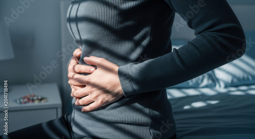 Woman Experiencing Stomach Pain, Holding Abdomen In Bedroom Under Dim Light