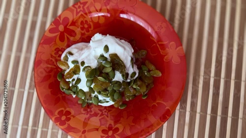 Homemade cottage cheese with yellow raisins and pumpkin seeds in a red glass plate on a bamboo background. Close-up