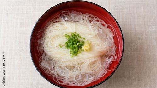 A lacquer bowl filled with ice water and noodles, garnished with green onion and ginger.