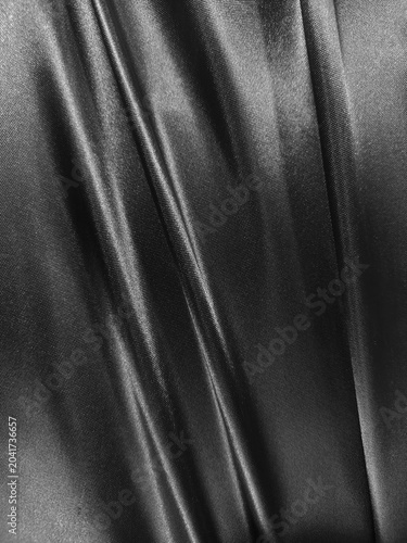 Luxurious black satin fabric flows with elegant folds, creating a sleek and sophisticated texture full of depth and shine.