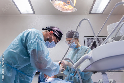 Fotografie Low angle view of dentist and assistant performing oral surgery in a clinic, wit