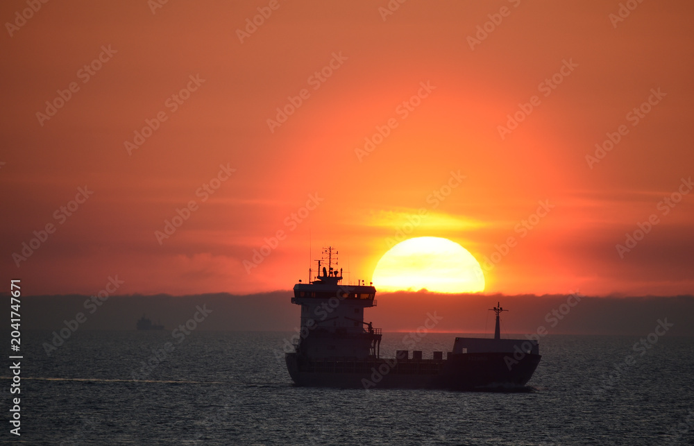 Obraz premium Frachtschiff fährt bei Sonnenaufgang in der Ostsee
