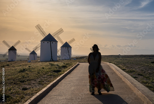 Schilderij op canvas Woman walking toward historic windmills at sunset in Campo de Criptana, a famous destination in Castilla-La Mancha known for its connection to Don Quixote and Spanish cultural heritage