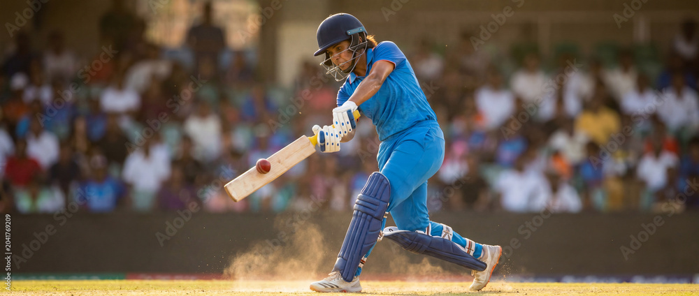 Naklejka premium Female cricket batter playing powerful shot in blue uniform on dusty field. Concept of women cricket, match action, athlete confidence, sports campaign, team training and tournament promotion.