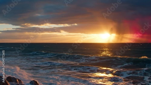 Ocean waves crashing against rocks at sunset, dramatic sky and beautiful golden hour light over the sea