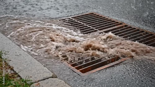 Heavy rainfall causes overflowing water to surge through street drain, capturing the power of nature's downpour