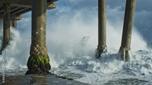 Powerful waves crash against the concrete pillars of a pier on a stormy day, ocean nature scene