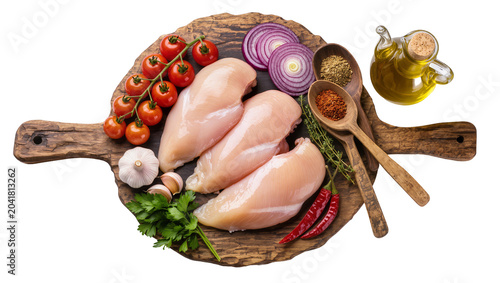 Raw chicken breasts with cherry tomatoes garlic red onion chili peppers herbs spices, and olive oil on a wooden board